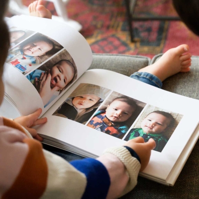 Children looking through an open printed hardcover photo book filled with baby photos