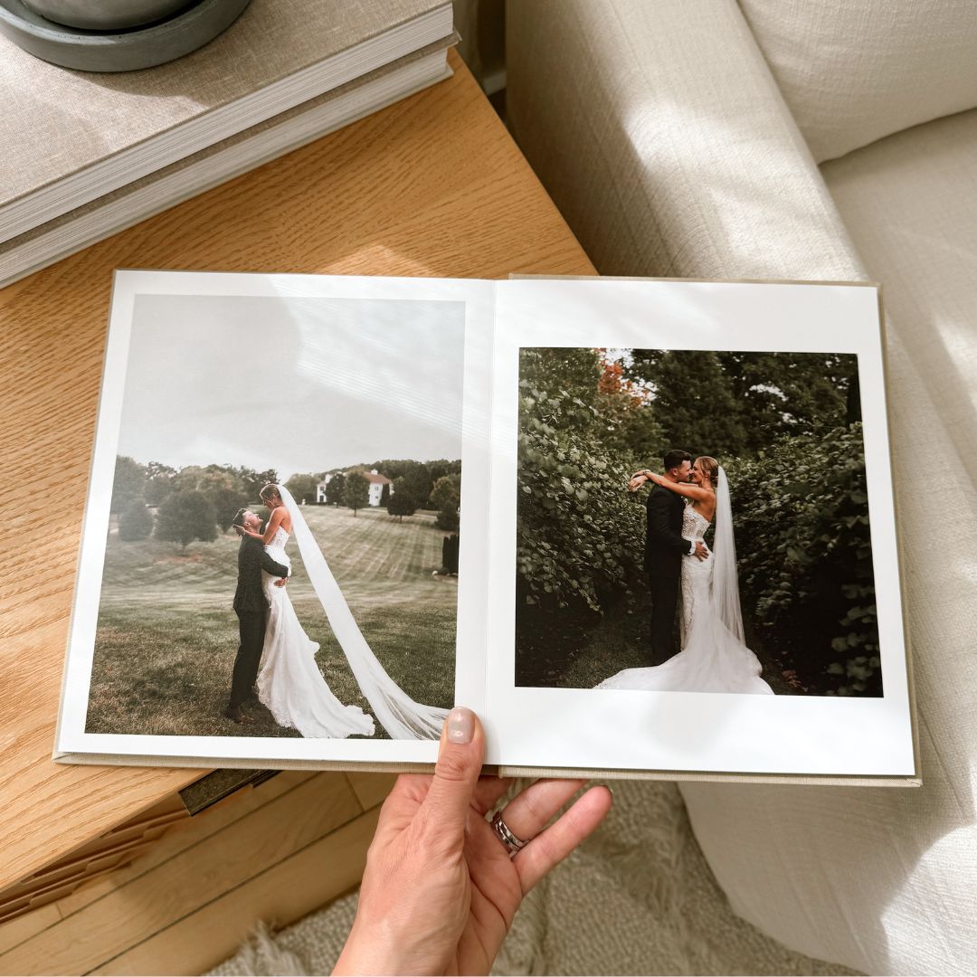 Layflat wedding photo album open on a wooden table, showing a bride and groom embracing outdoors, printed on thick white pages in a luxury linen wedding album.