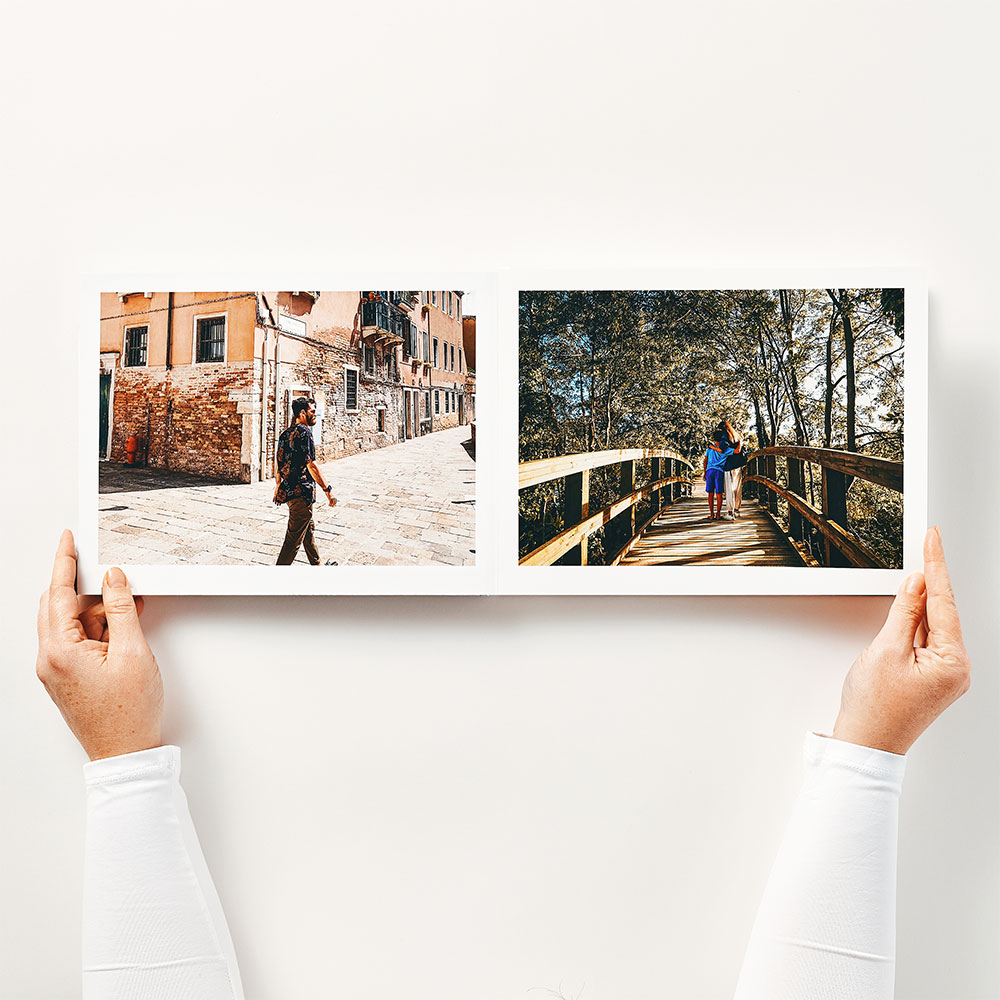 Hands holding an open layflat next day photo book from Inkifi, showing travel photos printed across two seamless pages on premium photo paper.