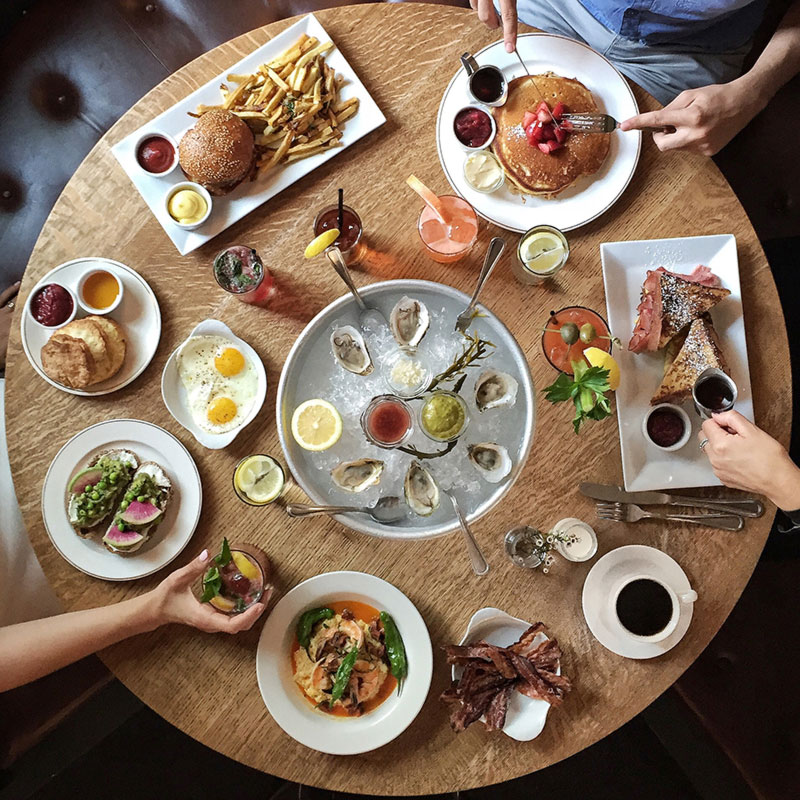 An image taken overhead using a mobile phone has used natural light to improve the quality of the iphone photography. The image shows 6 meals on a round table with drinks in the middle.