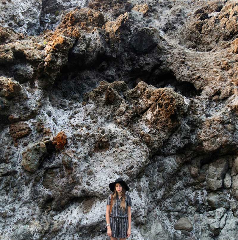 Image taken on an iphone shows a woman in front of a rock face. This image is before after have taken place. After edits, the colors of the rock are more defied.