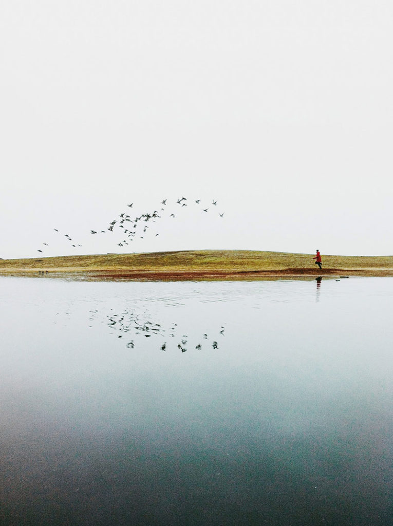 Image shows the value of iphoone photography tip less is more. Image is a landscape image with one man in a red coat and some birds flying overhead.