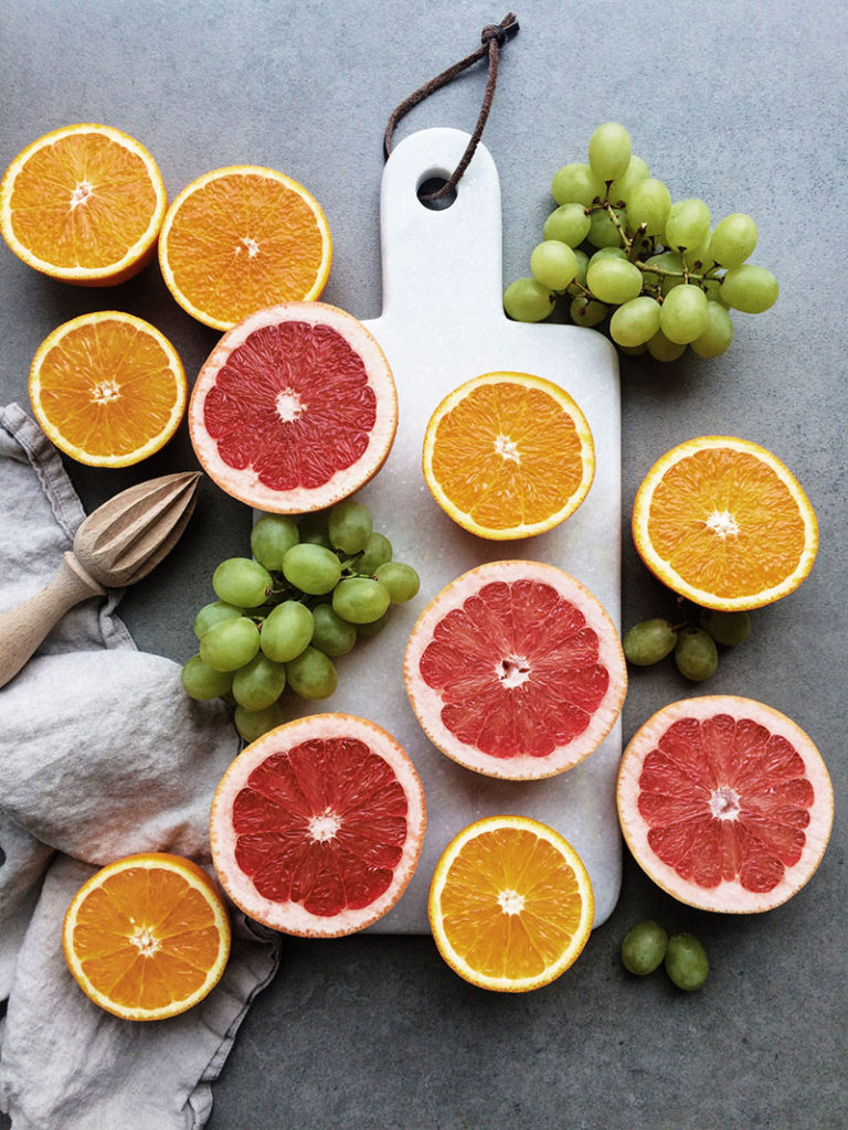 Natural light has been used in this iphone photography. The image shows oranges, grapefruits and grapes on a white chopping board.