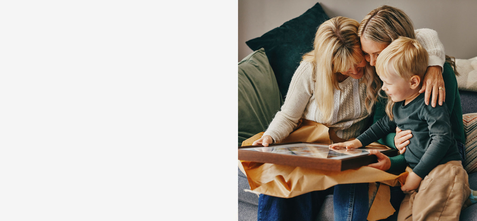Large wood-framed photo collage with a grid of small family images, wrapped with a ribbon and placed under a Christmas tree on a cozy wooden floor